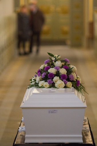 A vertical shot of a flower over a white casket with a blurred background