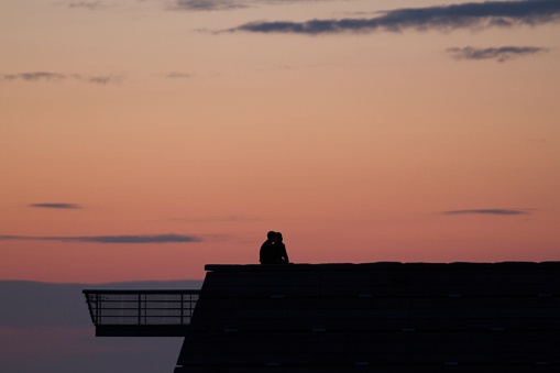 A silhouette of a romantic couple kissing on the roof during sunset