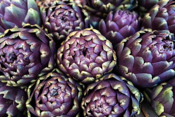 colpo ravvicinato di carciofi viola ordinatamente impilati in un mercato - purple artichoke foto e immagini stock