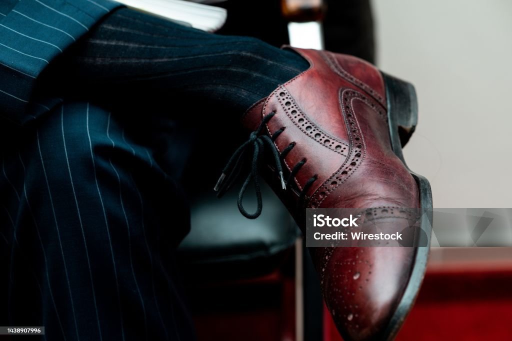 Closeup of a brogue shoe on a person sitting with crossed legs under the lights A closeup of a brogue shoe on a person sitting with crossed legs under the lights Brogue Stock Photo