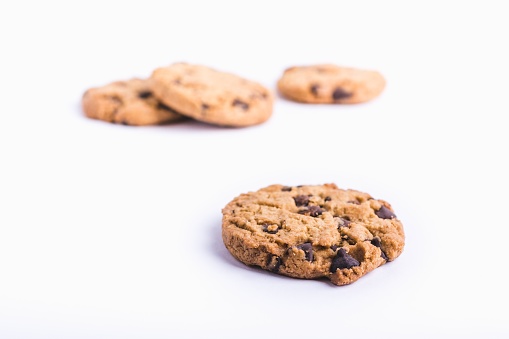 A closeup shot of a chocolate chip cookie with cookies in a blurred white background