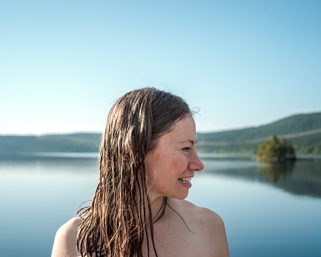 A smiling woman with wet hair surrounded by the lake and hills under the sunlight