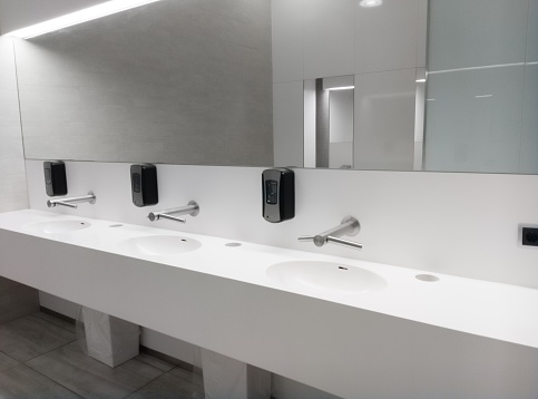 A modern public bathroom with white interior and a mirror with sinks