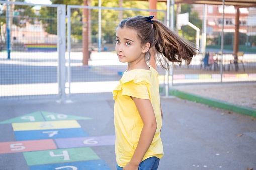 A rear view of a girl with a yellow shirt and hait tails playing hopscotch in the playground