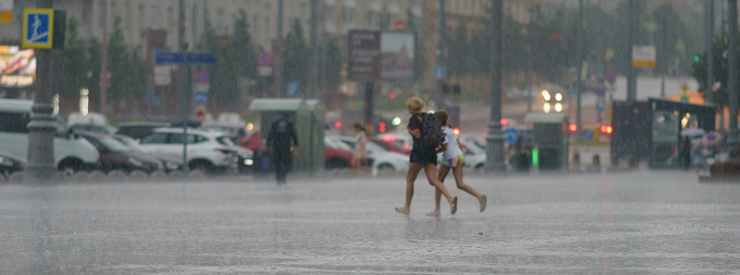 Moscow, Russia - July 10, 2022: Rainy day in city at summer. Mother with daughter running cross the street. Texture of strong, fresh and powerful water drops and sprays. Tropical storm. Panorama