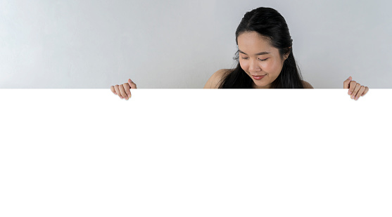 A cute beautiful woman holding a sign on a white background. Look down and look. Smiling woman holding a long blank white horizontal banner banner gray background