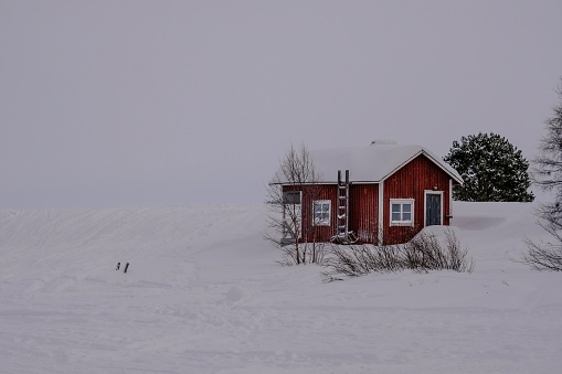 A small lonely wooden red house in the valley covered by snow in winter