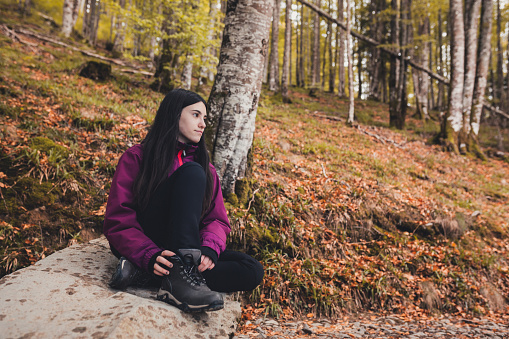Happy girl resting on a fallen beech tree while hiking through the forest in Autumn.  Active lifestyle concept.