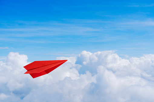 Paper red planes in blue sky. Sky background. The atmosphere is on the plane, sky is full of clouds floating around, both small and large. The atmosphere is on the plane.
