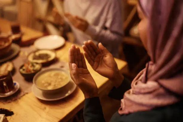 Close up of Middle Eastern woman and her family praying while having meal at dining table.