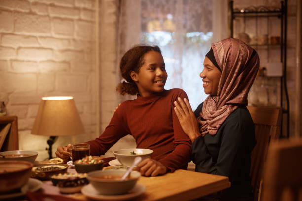 istock Happy black Muslim mother and daughter talking at dining table. 1438924021