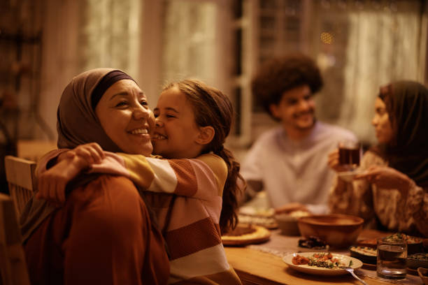 Happy Muslim little girl embracing her grandmother in dining room. stock photo