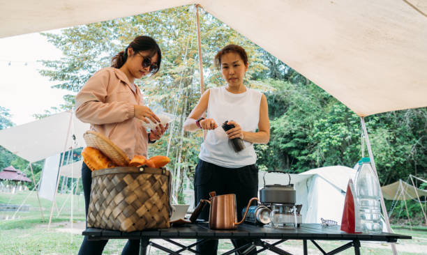 istock Beautiful two Asian Chinese female make coffee and using hand grinding roasted coffee bean with a hand grinder coffee at campsite. 1438924786