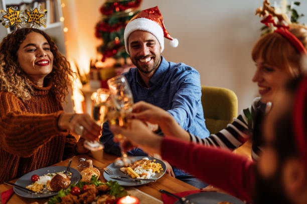 Group of diverse mid adult friends at home on Christmas night, eating dinner and drinking champagne stock photo