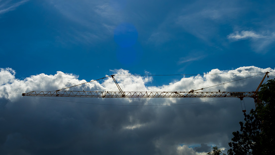 Sky sights, crane beam over a sunlit dark cloud in blue sky. construction site