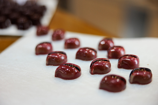 Dark chocolate truffles with red wine color glaze, in leaf shape and crack in the middle, served on white tray