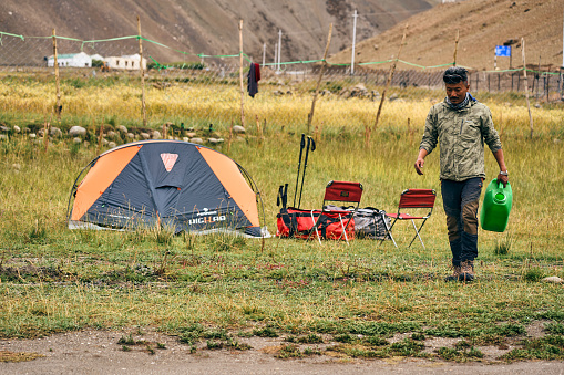 Leh, India, August 12th, 2022: Local man walking beside a tent holding a plastic tank