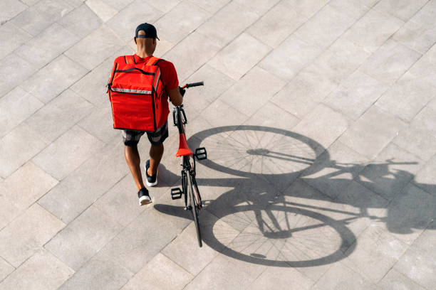 Messenger Man Using Bike Unrecognized african delivery man using his bike in the city in his way to deliver a package. top view on people walking and cyclists riding stock pictures, royalty-free photos & images