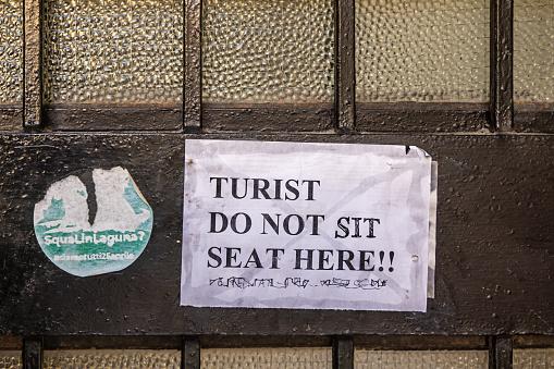 Venice, Italy - October 8th 2022:  Small poster telling tourists to move on in the center of the old and famous Italian city Venice where tourism is a expanding problem
