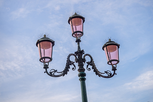Decorative forged street lamp in Mykolaiv, Ukraine. Antique metal streetlight with three lamps close-up, isolated on blue sky background