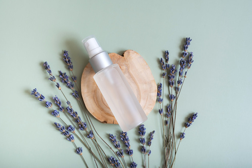 Cosmetic spray bottle on wooden slice  top view, flat lay on colored background with lavender flowers. Natural cosmetic concept