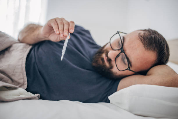 istock Male patient lying in the hospital bed and measuring temperature with thermometer 1438936607