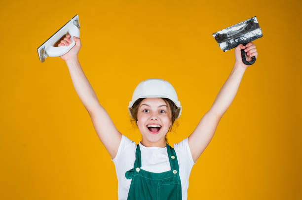 istock After the work is done. kid bricklayer masonry worker with helmet and putty knife. house renovation. happy girl working with spatula. small builder using putty knife. kid with helmet holding spatula 1438936654