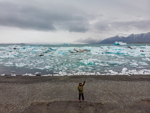 Woman with arm up while flying drone on glacier