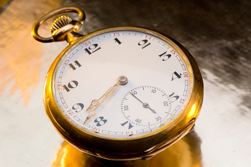Antique early 20th century gold, open-faced, Waltham pocket watch. The gold and white enamel watch face reads 5:55 with an additional seconds dial at 30 seconds. The outer gold base has intricate gold detailing and a top winding stem with a fob chain attached. This beautiful vintage timepiece is isolated on a white background.
