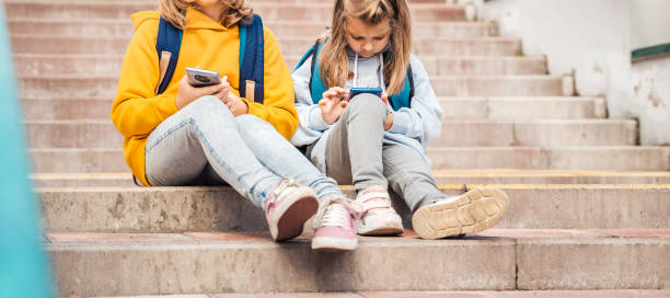 istock Back to elementary,primary school. Little girls with backpack,mobile phone.Chat, talk with mom,friends, classmates on break.Autumn study after vacation. Education of children.Pupil kid on stair steps 1438948698