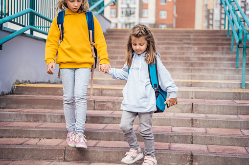 Back to elementary,primary school.Little girls,sisters with big backpacks go in hurry,late to first grade alone in autumn morning.Education,future of children.Happy,unhappy pupils kids on stair steps.