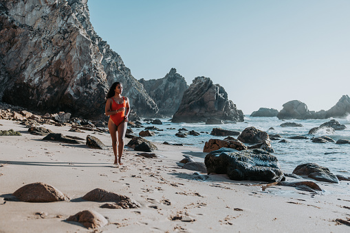 Portrait of a young women in red swimsuit running on  Ursa beach in Portugal on sunny day