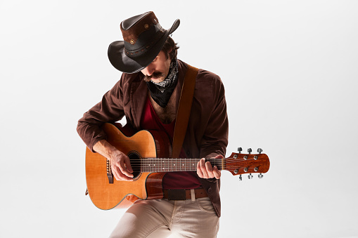 Portrait of man with moustaches in country style clothes playing guitar isolated over white background. Romantic music. Concept of music, creativity, inspiration, hobby, lifestyle, emotions