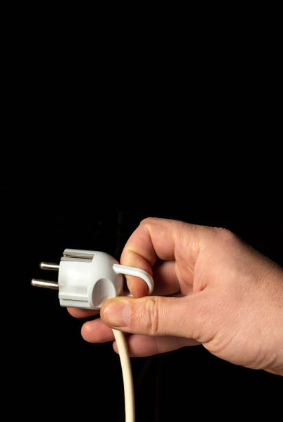istock Man hand plug in power plug close up on black background 1438951114