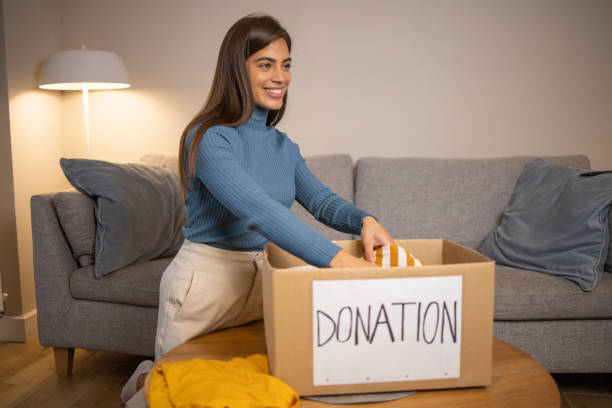 istock Young woman sorting clothing and packing donation box 1438951657