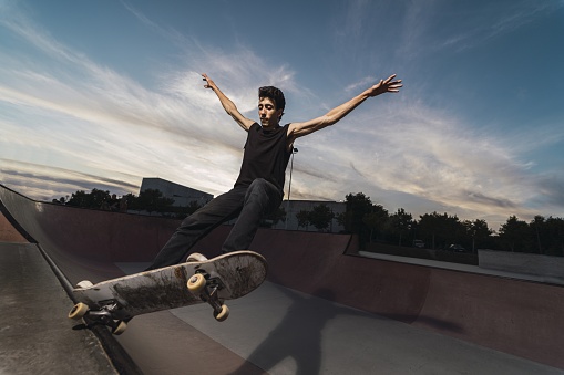 A low angle shot of a Caucasian athletic male in a black outfit doing a flip trick with a skateboard with wide open hands