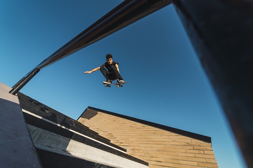 A low angle shot of a Caucasian athletic male in a black outfit doing a flip trick with a skateboard