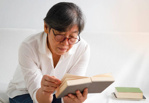 istock Old smart lady reading book for relax time at living room, 1438952525