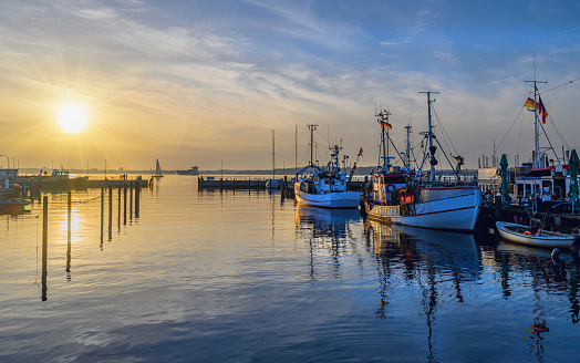 Fishing cutters and fishing boats stowed at the pier, lit by evening sun.Sunset over small harbor with fishing boats, cargo ship and sailing boat on the Kiel Fjord by Heikendorf,Schleswig-Holstein.