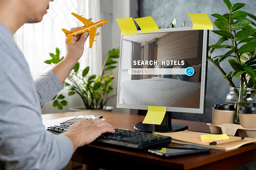 Man searching hotel using laptop at table, In his hand is a model of an airplane. Booking online service. Holiday booking online. Concept of modern travel agency web site