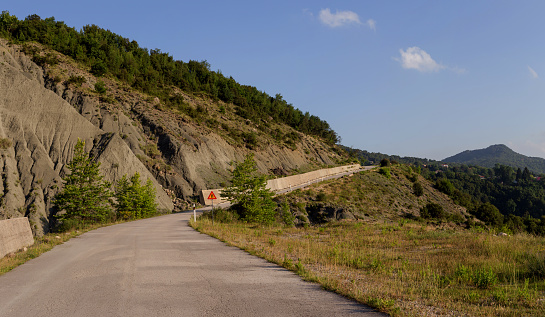 View of a rural road, sign narrowing of the road and mountains on a sunny, summer day (region Tzoumerka, Epirus, Greece).