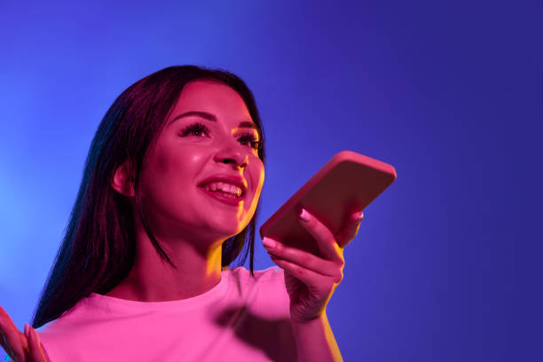 istock Using phone, astonished. Caucasian woman's portrait isolated on gradient studio background in neon light. Beautiful female model. Concept of human emotions, facial expression, sales, ad. 1438959397