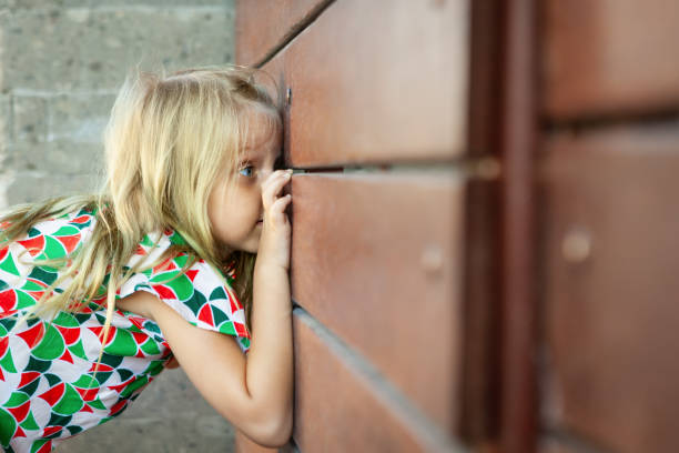 門のスリットを覗き込む少女。家族のライフスタイル。 - fence child neighbor peeking ストックフォトと画像