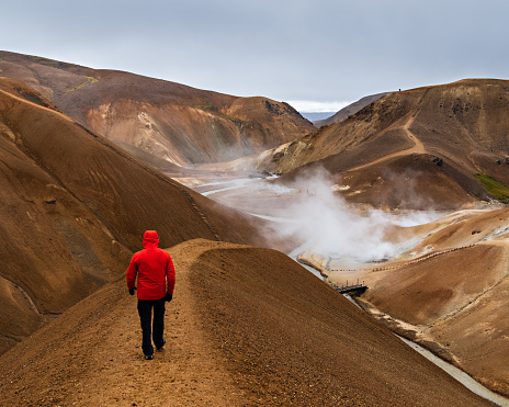 The behind shot of a man in a red coat walking through the hills of Highland region, Iceland