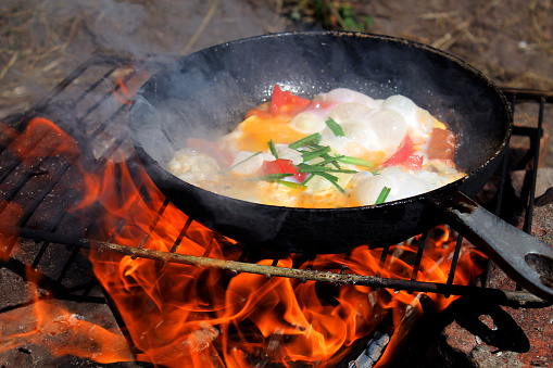 fried eggs on a campfire in the forest, fried eggs on a campfire on a camping trip, scrambled eggs in a frying pan on fire, cook an omelet on a fire, Cooking on a campfire, breakfast on the fire