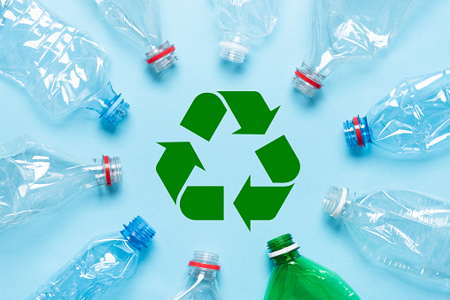 Empty crumpled plastic bottles on blue background with recycle symbol in center