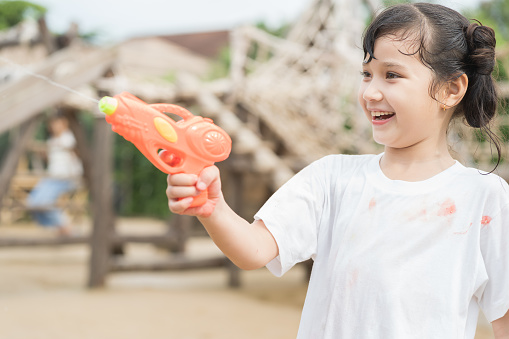 Asian girl playing with water gun on hot summer day outdoors. Kid girl having fun with water outdoors