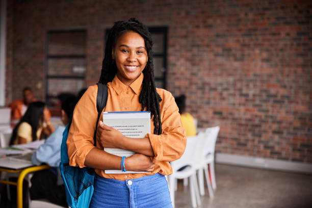 istock Young female college student smiling while standing with books in a classroom 1438965911