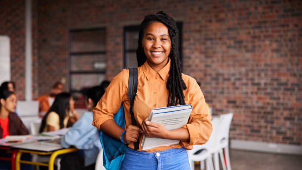 istock Young female college student smiling while standing with books in a classroom 1438966134