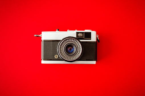 An analog vintage 35mm film camera on a bold red background.